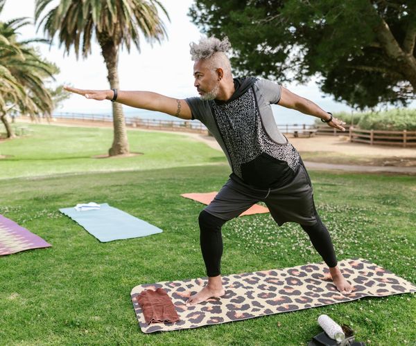 Vibrant senior man performing a light stretching exercise in a green park.